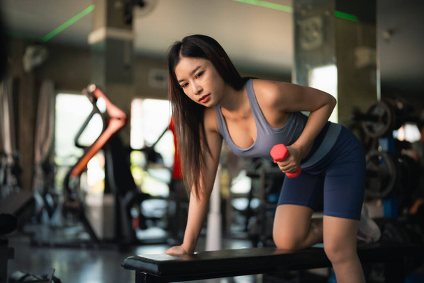 Ázsiai fitt sportos nő mosolyog és gyakorló súlyokat súlyzózik súlyzókkal a fitneszteremben. Sportruhát viselő ázsiai nő tornázik, hogy zsírt égessen a tornateremben. Sport nő fitness koncepció. - Fotó, kép