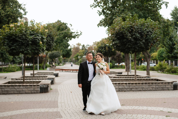 the groom in a brown suit and the bride in a white dress in an urban atmosphere - Fotoğraf, Görsel