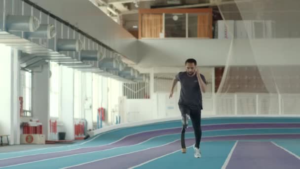 Langzame professionele para-atleet met hardloopmes op zijn geamputeerde ledemaat joggen op de baan in het indoor stadion - Video