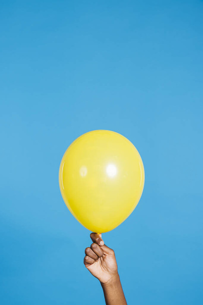 Primo piano della mano della donna che tiene un palloncino giallo davanti allo sfondo blu in uno studio. Donna con un palloncino giallo. - Foto, immagini
