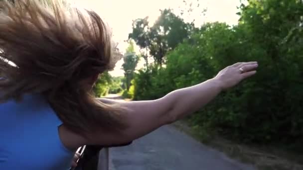 Mujer inclinada por la ventana del coche y sosteniendo su mano mientras pasea por el camino del campo. Chica mirando por la ventana de movimiento automático y disfrutar del viaje. Concepto de viaje o viaje por carretera. Lento mo. - Metraje, vídeo