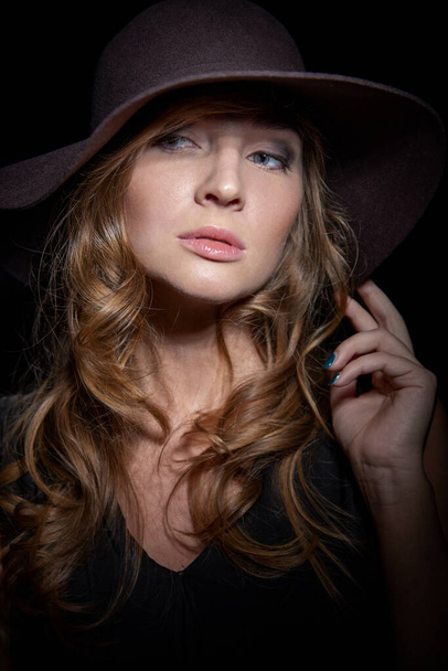 Femme sexy à la mode dans un chapeau élégant et robe noire. Mystérieuse blonde dans un style rétro sur fond noir. - Photo, image