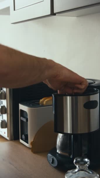 Vertikální bodnutí boční záběr nerozpoznatelné mužské ruce nakládání kávovar s mletou kávou a zapnutí v moderní domácí kuchyni - Záběry, video
