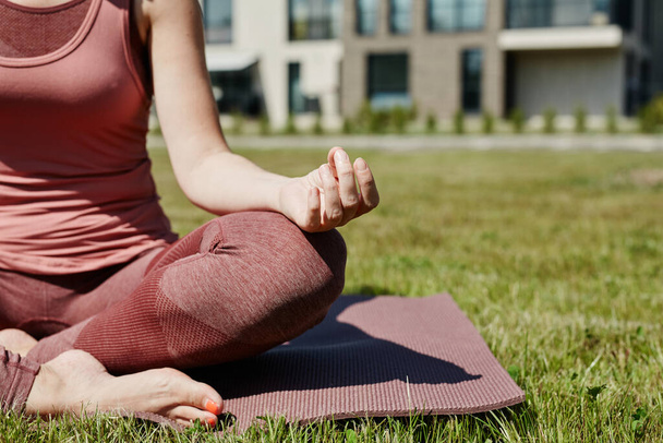 Primo piano di giovane donna seduta in posizione di loto illuminata dalla luce solare mentre si gode lo yoga all'aperto su erba verde, copiare lo spazio - Foto, immagini