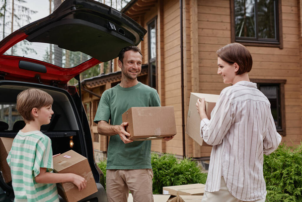 Portret van gelukkige familie lossen dozen uit auto kofferbak, terwijl verhuizen naar een nieuw huis in de natuur - Foto, afbeelding