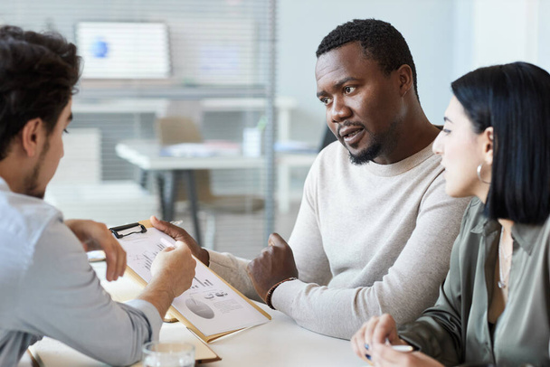 Portrait of black man holding clipboard while discussing project in business meeting with team - Photo, Image