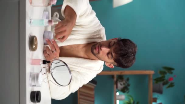 Handsome young man in bathrobe apply eye patches with collagen at home interior. Morning daily beauty procedures. Male Skincare and rejuvenation concept. Vertical video - Footage, Video
