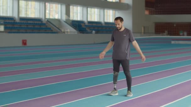 Täysi kuva nuori valkoihoinen mies urheilija proteesi osa tekee kehon ja käsivarren kierrosta lämpenee harjoituksen aikana sisätiloissa radalla stadionilla - Materiaali, video