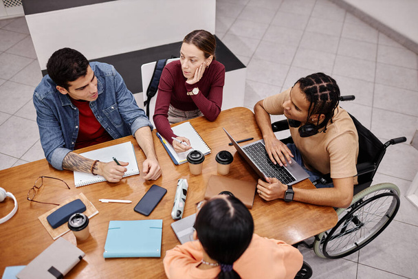 Вид сверху на группу молодых людей, которые вместе учатся за столом в библиотеке колледжа, концепция инклюзивности - Фото, изображение
