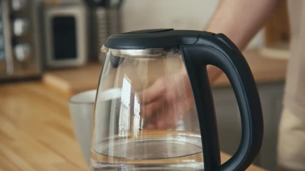 Stab side shot van onherkenbare man het inschakelen van de elektrische waterkoker op de knop en weg te gaan in de moderne keuken - Video