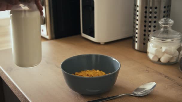 Stab lado tiro de mão derramando leite em tigela de cereal saudável em mesa de madeira na cozinha moderna - Filmagem, Vídeo