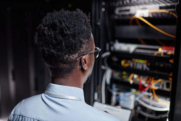 Takaisin näkymä musta mies verkko-insinööri työskentelee palvelimen kaappi datakeskuksessa, kopioi tilaa - Valokuva, kuva