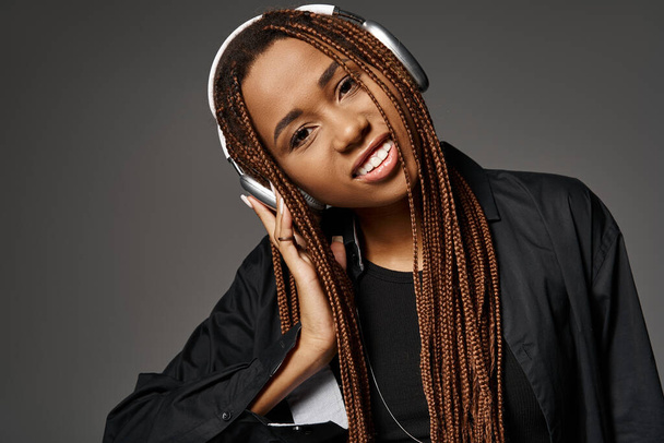 retrato de chica afroamericana feliz en rastas escuchando música en auriculares inalámbricos en gris - Foto, imagen
