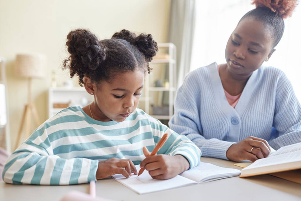 Retrato de menina negra bonito estudando em casa com mãe carinhosa ou tutor ajudando - Foto, Imagem