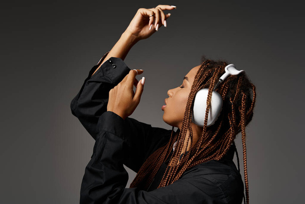artistiek afrikaans amerikaans meisje in de 20 met dreadlocks luisteren muziek in hoofdtelefoon op grijze achtergrond - Foto, afbeelding