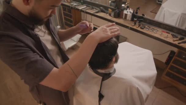 Alto ángulo de tiro de peluquero profesional peinando el pelo mojado del cliente, mientras que le da corte de pelo en el salón - Imágenes, Vídeo