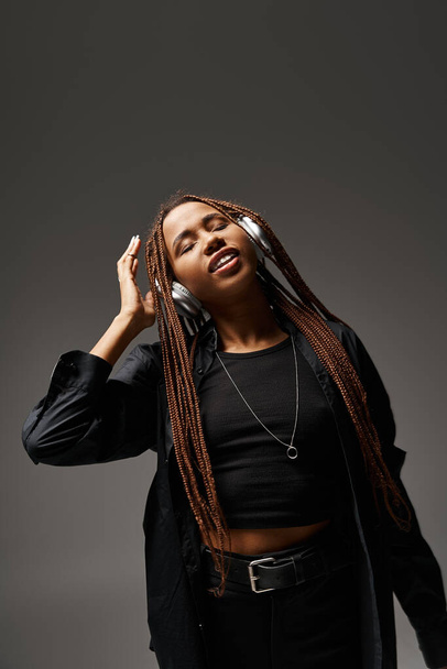 20 'li yaşlarda Afrikalı Amerikalı bir kız Rastalı saçlarıyla gri arka planda kulaklıkla müzik dinliyor. - Fotoğraf, Görsel