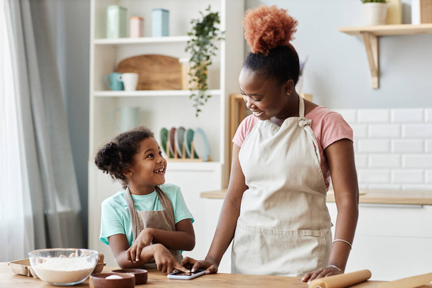 Cintura até retrato de mãe negra feliz e filha cozinhar juntos na cozinha acolhedora e vestindo aventais - Foto, Imagem