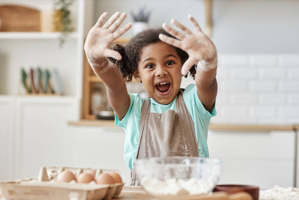 Porträt eines glücklichen schwarzen Mädchens, das das Backen in der Küche genießt und der Kamera Hände mit Mehl zeigt, Kopierraum - Foto, Bild
