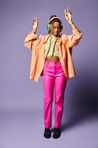 紫色のヘッドフォンで活気に満ちた服装で陽気なアフリカ系アメリカ人の少女の静かなダンス - 写真・画像