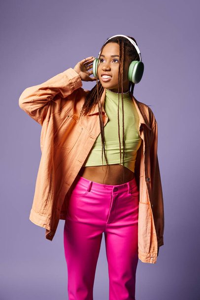 stylový šťastný africký americký žena v živé oblečení s bezdrátovými sluchátky na fialovém pozadí - Fotografie, Obrázek