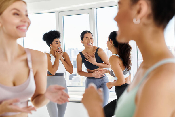 focus on diverse female friends in sportswear laughing while chatting before pilates class - Photo, Image