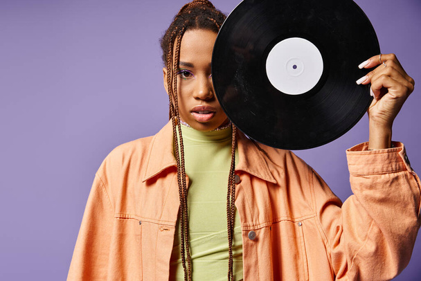 african american woman in her 20s with dreadlocks covering half of face with vinyl disc on purple - Photo, Image