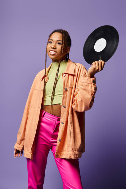 feliz joven afroamericana chica en sus años 20 con rastas sosteniendo disco de vinilo sobre fondo púrpura - Foto, Imagen