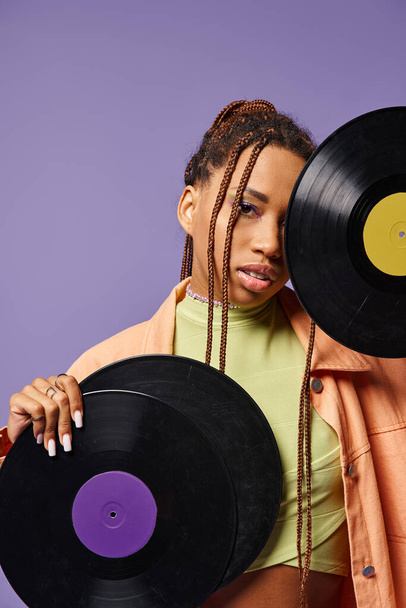 young african american girl in her 20s with dreadlocks posing with vinyl discs on purple backdrop - Photo, Image