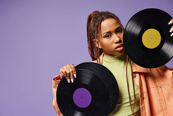 young african american woman in her 20s with dreadlocks posing with vinyl discs on purple backdrop - Photo, Image
