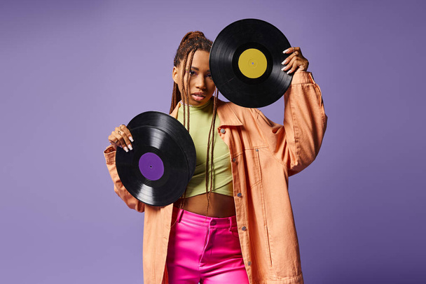 stylowa Afroamerykanka w wieku 20 lat z dredami pozującymi z płytami winylowymi na fioletowym tle - Zdjęcie, obraz