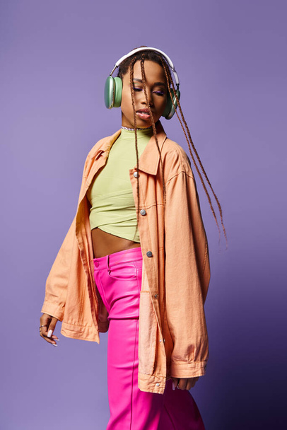 alluring african american woman in 20s listening music in wireless headphones and walking on purple - Zdjęcie, obraz
