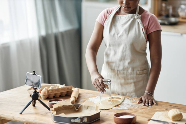 Przycięte ujęcie czarnej kobiety pieczenia domowego ciasta w kuchni domowej z aparatem fotograficznym smartfona nagrywania wideo lub livestream, przestrzeń kopiowania - Zdjęcie, obraz