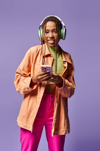 happy african american woman in green wireless headphones using smartphone on lilac backdrop - Photo, Image