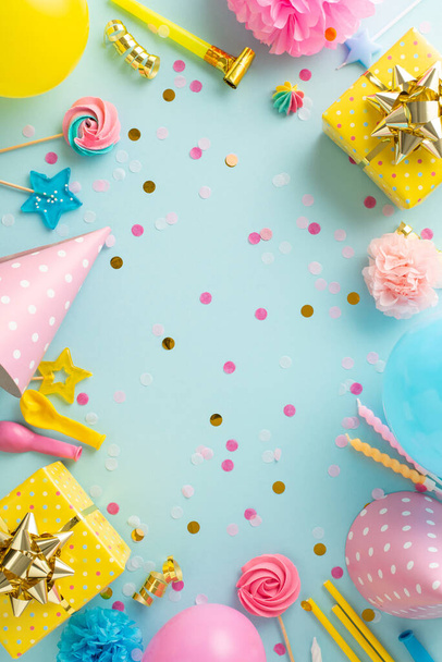 Exciting birthday concept composition. Overhead vertical image of festively decorated table with gifts, birthday hats, balloons, confetti, and more against soft blue backdrop. Ideal for text or advert - Photo, Image