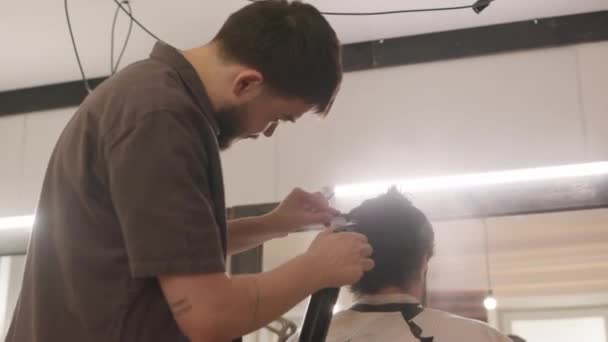 Barber ruiskuttamalla hiukset mies asiakkaan vedellä ja harjaamalla kampa valmistellessaan leikata hiukset - Materiaali, video