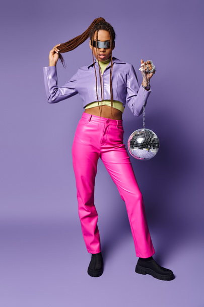 african american girl in futuristic sunglasses and headphones standing with disco ball on purple - Photo, Image