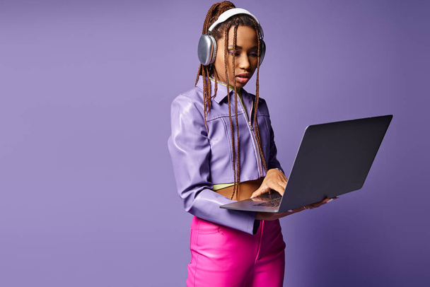 Африканская женщина с наушниками, работающая на ноутбуке удаленно на фиолетовом фоне - Фото, изображение