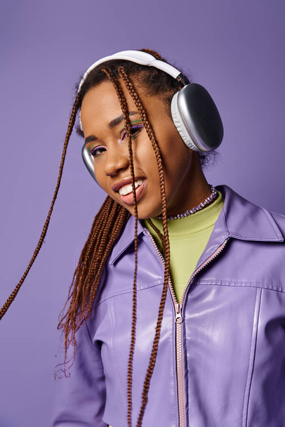 Sonriente joven afroamericana con auriculares inalámbricos disfrutando de música sobre fondo púrpura - Foto, imagen