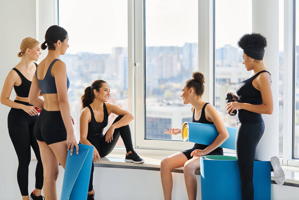 felizes multiculturais jovens mulheres em 20s conversando enquanto sentado ao lado da janela no estúdio de ioga - Foto, Imagem