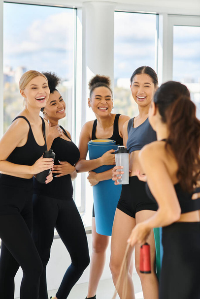 five young multicultural women in active wear chatting and laughing after workout in pilates studio - Photo, Image