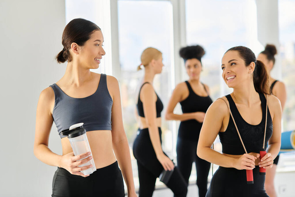 cheerful multicultural female friends in active wear smiling at each other after pilates workout - Photo, Image