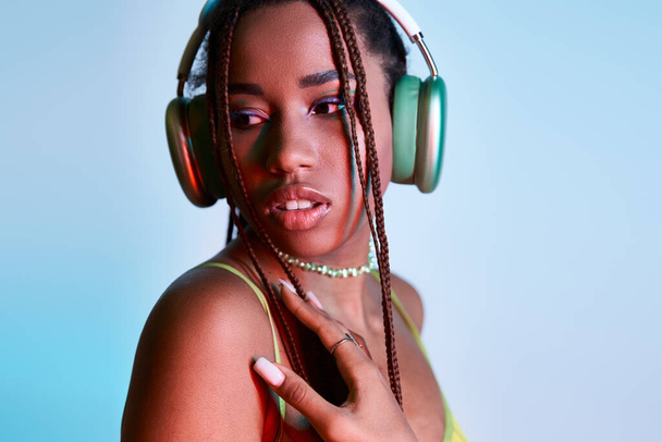 verträumte afrikanisch-amerikanische Frau mit Dreadlocks in drahtlosen Kopfhörern schaut in die Kamera auf blau - Foto, Bild