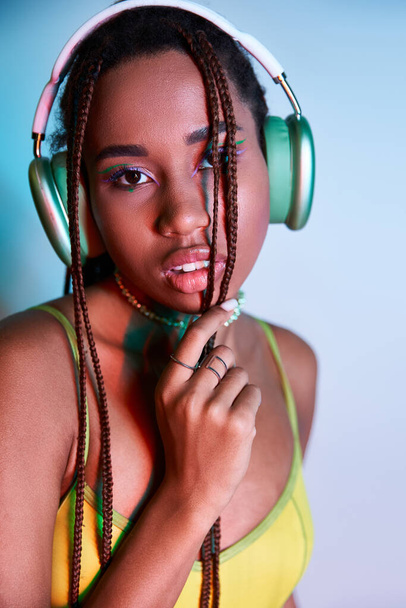 alluring african american woman with dreadlocks in wireless headphones looking at camera on blue - Photo, image