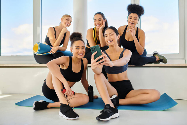 skupina pěti a veselých mezirasových kamarádek ve sportovním oblečení při selfie po hodině jógy - Fotografie, Obrázek