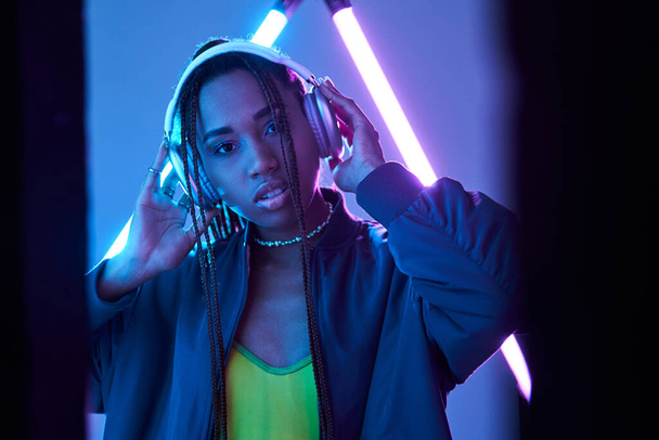 όμορφη αφρικανή αμερικανίδα με ακουστικά που απολαμβάνει μουσική στο στούντιο με φθορίζον φως - Φωτογραφία, εικόνα