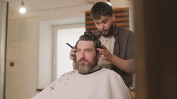 Berber kuaförde saçını kestirirken erkek müşterinin saçını suyla tarayıp spreyliyor. - Video, Çekim