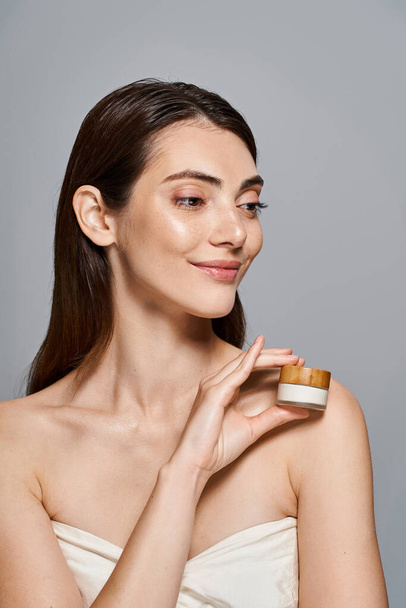 A young happy woman delicately holds a jar of cream, exuding purity and beauty. - Photo, Image