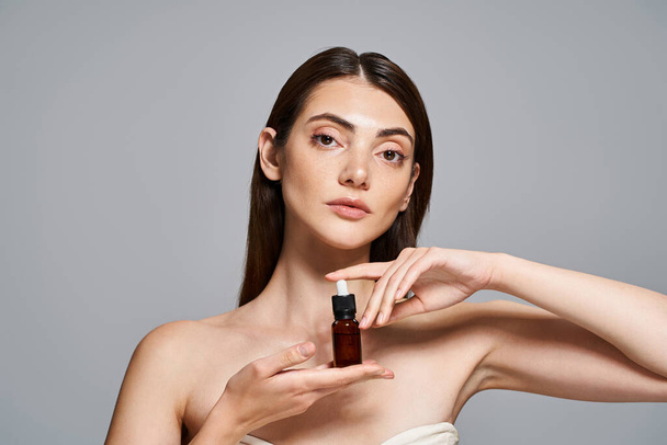 Egy fiatal kaukázusi nő barna hajjal, kezében egy üveg bőrápolási termékkel, ragyogó és egészséges arcbőrt mutatva. - Fotó, kép