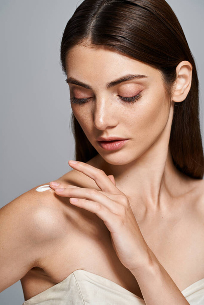 A young woman with brunette hair poses gracefully in a strapless dress, her hands delicately touching cream on shoulder - Photo, Image